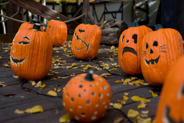 Carved Halloween pumpkins with different funny and scary faces on a wooden deck covered with autumn leaves, glowing jack-o'-lanterns decoration for spooky fall celebration.