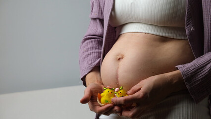 Women belly, pregnant woman hold cute yellow chicken near abdomen.