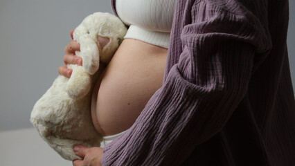 Women belly, pregnant woman hold cute baby rabbit near abdomen.