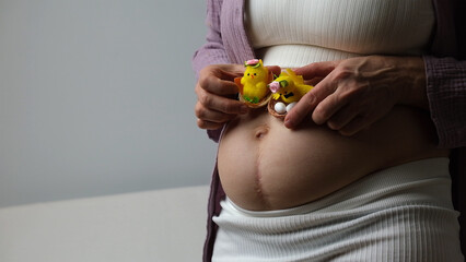 Women belly, pregnant woman hold cute yellow chicken near abdomen.