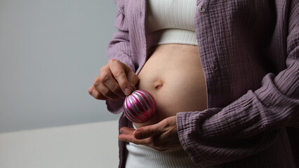 Women belly, pregnant woman hold Christmas tree toy near abdomen.