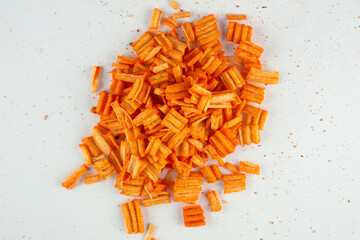 Close-up of a pile of orange, ridged, crunchy snacks on a white surface. The small, textured pieces...