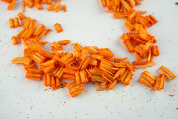 Close-up of crunchy orange ridged snacks scattered on a white surface. The small, crispy pieces are...