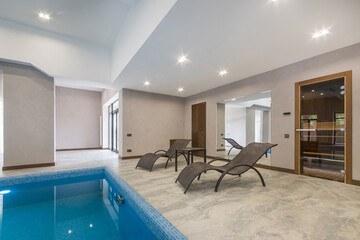 An elegant spa area with a swimming pool, lounge chairs, a sauna behind a glass door and stylish lighting.