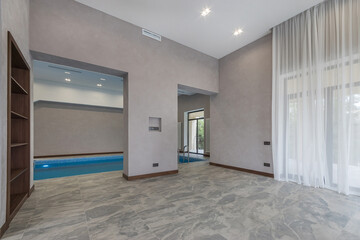 A spacious, bright hall with large windows and a swimming pool in the interior of a country house.