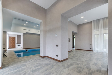Modern interior design with swimming pool and spacious living space in a luxury house. Natural light penetrates through the large windows, creating a cozy atmosphere.