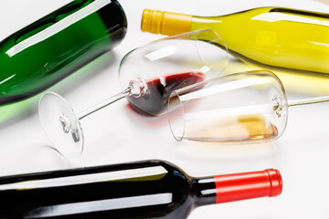 Wine glasses with red and white wine and bottles lying on white background