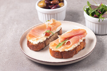 Two bruschettas with prosciutto, ricotta cheese and rucola on ciabatta bread. Olive and spices  decorated.
