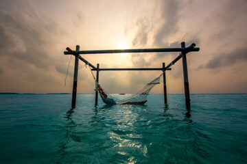 Fototapeta premium Tranquil closeup calm sea water waves with palm trees. Model sitting on hammock. Tropical island beach landscape exotic shore coast. Summer vacation, holiday amazing nature. Relax paradise, Maldives.