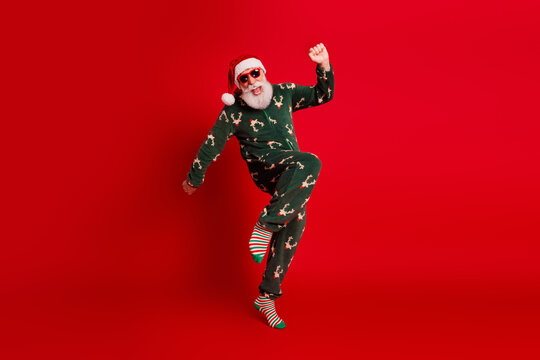 Funny santa in christmas pajama jumps against red background wearing sunglass for holiday party mood and festive dream