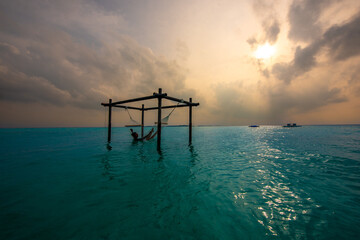 Tranquil closeup calm sea water waves with palm trees. Model sitting on hammock. Tropical island beach landscape exotic shore coast. Summer vacation, holiday amazing nature. Relax paradise, Maldives.