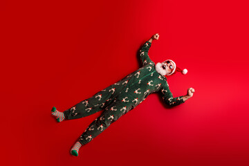 Joyful Santa in Christmas pajamas lies on red background posing for a playful holiday stock photo