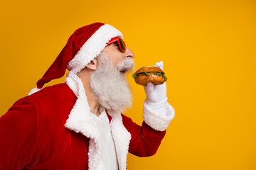 Festive Santa Claus enjoying a delicious burger while celebrating Christmas against vibrant yellow background
