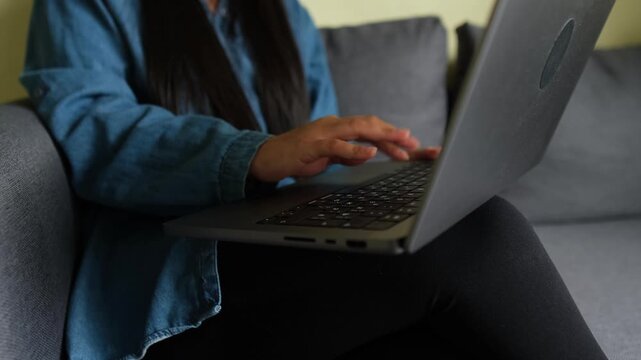 Woman typing on a laptop at home, simple lifestyle moment, casual remote work on the sofa.