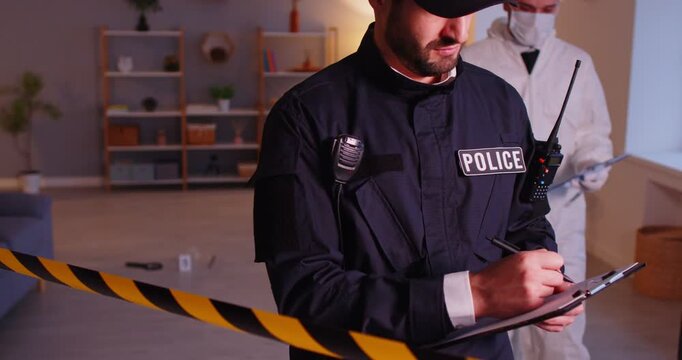 Policeman and CSI criminologist working together at a crime scene in a home, collecting evidence, investigating a murder, and following 911 procedures during a forensic examination.