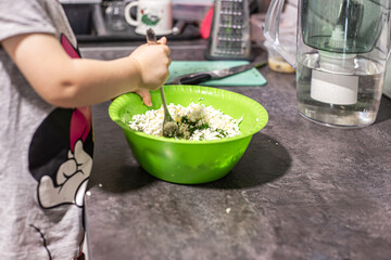 A small child helps cook in the kitchen by stirring trorog in a cup