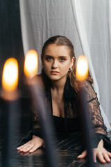 Mysterious young woman in black lace gazes intensely through candlelight, evoking elegance and gothic allure