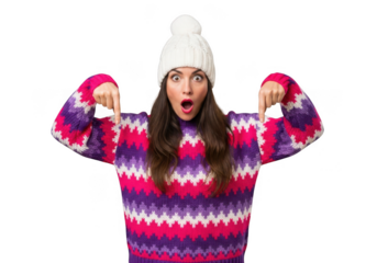 Young woman wearing a colorful striped sweater and white knitted hat, pointing down with a surprised expression, isolated on transparent background