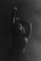 A mysterious woman stands in silhouette against a bright window, surrounded by dramatic smoke and shadows