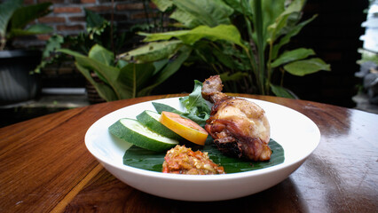 A delicious plate of grilled chicken served with fresh cucumber slices, tomato, and a side of sambal.