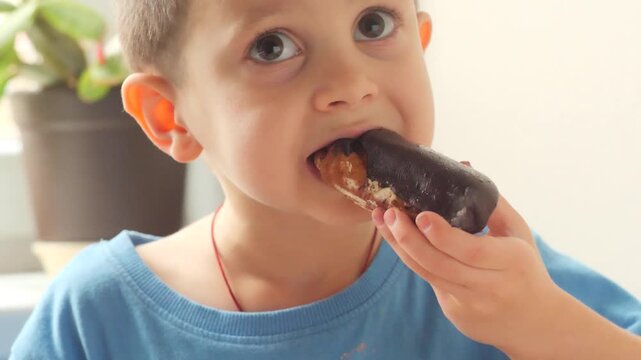 Young boy enjoying a bite of a chocolate eclair cake near a window.
