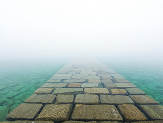 Stone pathway submerged in clear turquoise water fading into fog