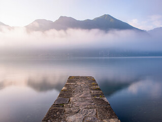 Stone pier extending into calm lake with misty mountains
