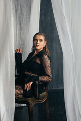 Confident woman in sheer black lace stands poised between white curtains, embodying strength, elegance, and modern gothic fashion