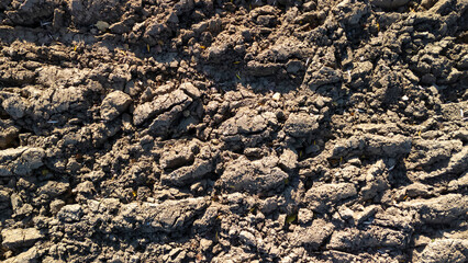 Close-up of uneven soil texture featuring dry, cracked earth with visible tire tracks and scattered debris, indicating agricultural work or land preparation.