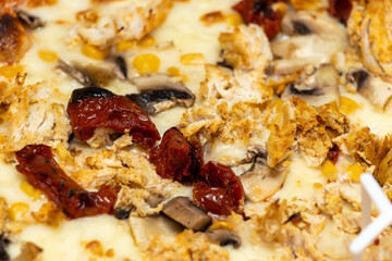 Delicious pizza topped with shredded chicken, sun-dried tomatoes, mushrooms, and corn, ready to be served for a satisfying meal at a gathering or pizza party.