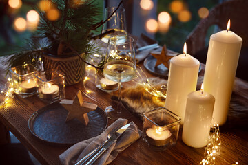 Elegant table decoration for a christmas dinner. Romantic dinner concept with burning candles in the evening at a restaurant. Close-up with golden bokeh lights.