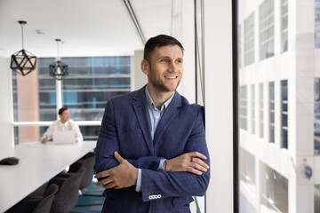 Fototapeta premium Positive young male company CEO man standing at large window