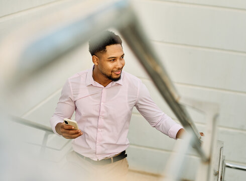 Portrait of a young businessman man using a smartphone mobile phone walking down the stairs, surrounded by moder corporate office buildings and modern city architecture