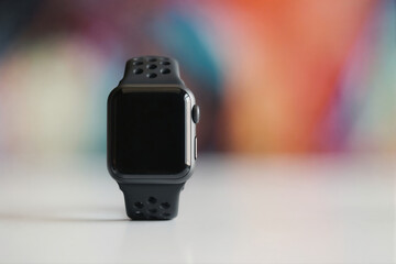 Modern black smartwatch on a white surface with a colorful background