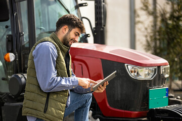 Young tractor driver using tablet beside tractor