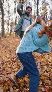 Young parents and little daughter laughing and throwing yellow foliage at each other, playing in forest. Sunny day, fall. Slow motion, dolly shot