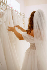 A rear view of a young woman in a wedding dress examining wedding gowns on display in a boutique