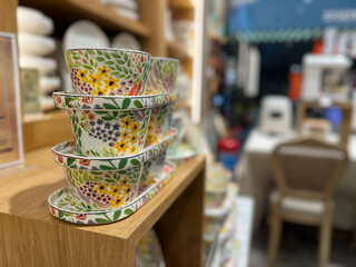 Colorful ceramic bowls and trays with yellow floral patterns stacked on a wooden shelf.