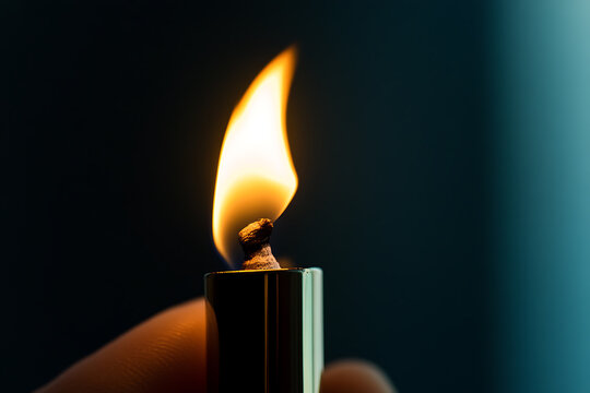 Close-up of a hand holding a metallic lighter with a flame burning against a dark, blurred background. The flame is the focal point, providing warmth and light in the darkness.