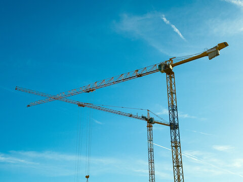 Two construction cranes against a bright blue sky. Industrial scene symbolizing modern construction, technology, and urban development - Powered by Adobe