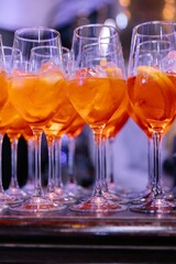 Row of elegant wine glasses filled with bright orange Aperol Spritz cocktails with ice and orange slices, set on a dark bar counter.