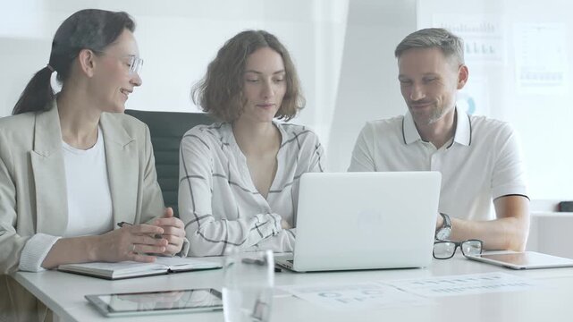Business professionals reviewing marketing analytics on laptops, working together strategically in contemporary workplace with minimalist interior design and collaborative atmosphere