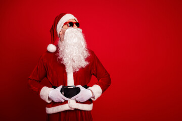 Santa in a red velvet suit with white beard and hat poses with belt and gloves on a bold red...