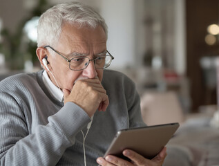 Intense Close-Up: Senior Man (80s) Pondering a Digital Strategy While Listening with Wired Earbuds and Looking at a Tablet