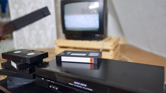 Hand takes a tape from the VHS recorder and puts into the player. Man pushes the button on the panel of the device. Close up.