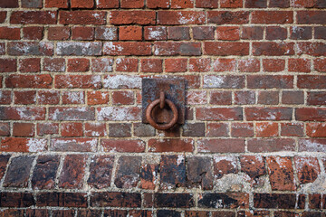 close up of a rusty metal ring mounted on a square plate against a weathered brick wall