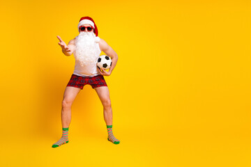 Santa in a playful home scene wearing a hat and beard with a soccer ball looks ready for a festive game against the bright yellow background
