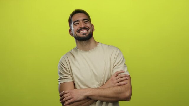 Young man smiling confidently with arms crossed in casual attire against vibrant yellow background portraying friendliness and positivity