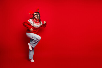 Playful holiday chic a young woman in a red sweater and jeans wearing festive accessories against a bright red background