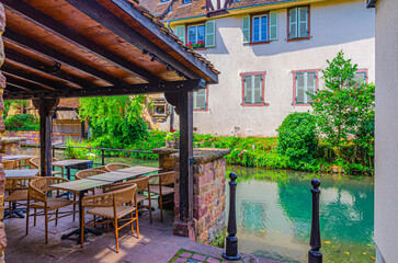Street restaurant on wooden terrace with tables and chairs on quay of river Lauch canal in Little Venice la Petite Venise area in old town Colmar city historic centre, Alsace Grand Est region, France